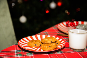 A festive scene featuring chocolate chip cookies on a red-and-white striped plate on plaid tablecloth