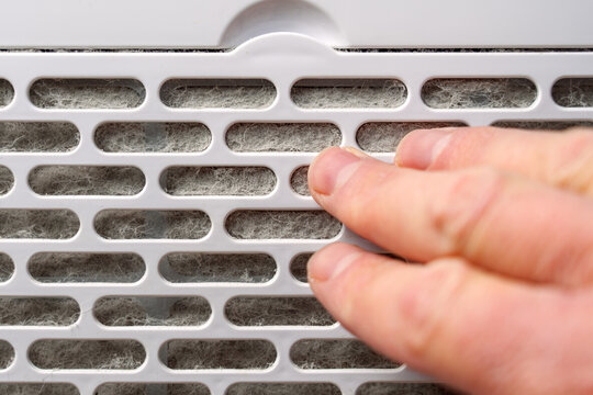 Dust clogged air purifier filter touched by human fingers. Allergy component. Household maintenance concept