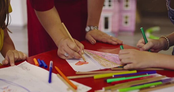 Creative kids during an art class in a daycare center or elementary school classroom drawing with female teacher. 