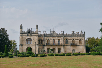 Fototapeta premium Castle building with ornate Gothic facade sits on a green lawn under a blue sky, showcasing historic architecture and tranquil landscape suitable for tourism.