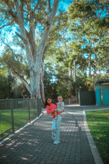 parent holding child, caretaker strolling with kid beneath and among tall eucalyptus trees