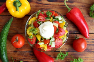 There is a glass plate with a fresh vegetable salad on the wooden table.	