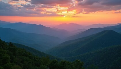 Hills and valleys fade into misty blue haze under vibrant sunset sky. Mountain layers glow with orange pink hues, tree covered slopes stand dark green.