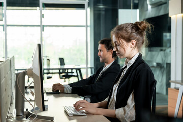 Young female and male coworkers sitting side by side working on desktop computers in office...