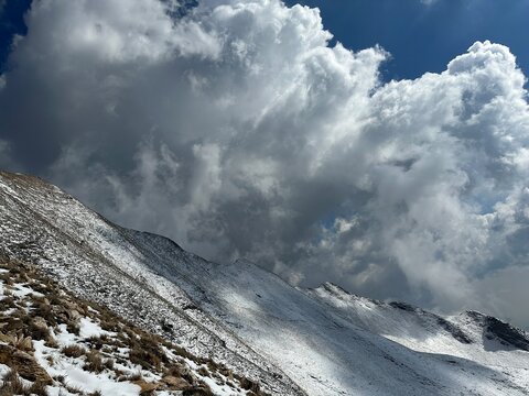 Snow-covered mountain landscape under a dramatic cloudy sky, showcasing natural beauty and serene outdoor scenery.