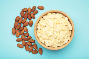 Fresh almond flakes and nuts in bowl on blue background