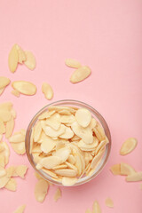 Fresh almond flakes in bowl on pink background. Vertical photo