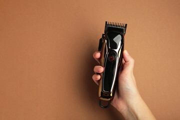 Hair clipper in hand on brown background. Modern hair clipper. Space for text
