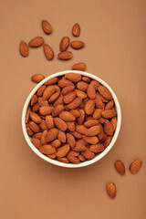 Almonds in bowl on brown background. Whole and dried nuts. Vertical photo