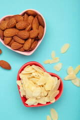 Fresh almond flakes and nuts in bowl on blue background. Vertical photo