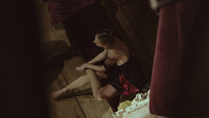 Ballet dancer resting on bench backstage between practice segments. Concept of break organization, costume readiness and workflow management during production preparations.