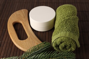 Natural spa tools arranged on a wooden surface with greenery, showing a towel, cream container, and massager