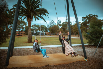 two friends enjoying sunny park day, two friends share joyful moment swinging under palm