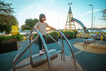 A young girl enjoys playing on a modern outdoor playground at sunset, highlighting fun and adventure.