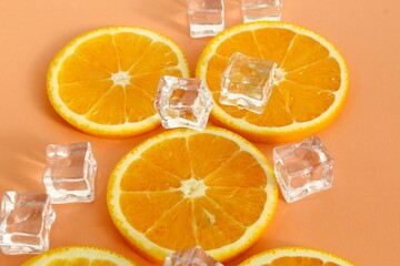 Sliced ​​oranges with ice cubes lie on a pink background.	