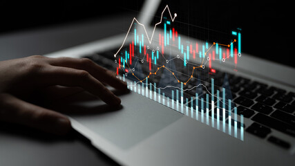 A striking image captures a hand interacting with a laptop, enhanced by vibrant trading graphs...