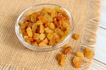 There is a glass bowl with yellow raisins on the wooden table.	