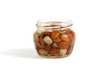 There is a glass jar with honey and nuts on a white background.	