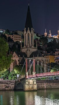 Timelapse hyperlapse of Saint George Church, Quais de Saone and Fourviere Basilica from a footbridge in Vieux Lyon, France, showcasing historic architecture at night, reflections and scenic river view