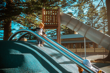 A joyful child slides down a fun slide at a beautiful playground with tall trees