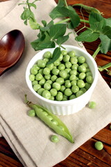 There is a wooden cup with green fresh peas on the wooden table.	