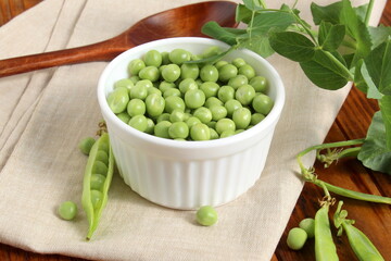 There is a wooden cup with green fresh peas on the wooden table.