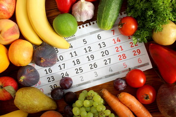 There are a lot of fresh vegetables and fruits on a calendar sheet on a wooden table.
