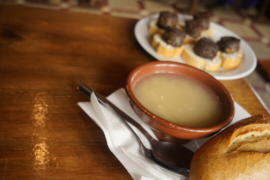Mesa de madera con comida en invierno de mundo rural en pueblo, cuenco de barro con sopa y plato de morcilla con pan