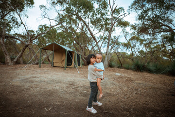 A child happily carries a toddler at a tranquil camping site nestled among lush green trees and nature