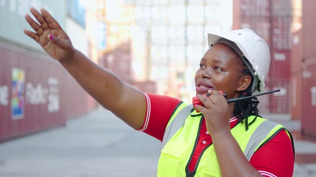 A female american african engineer engaged in effective communication with a forklift driver at a bustling shipping dock, using gestures and a walkie-talkie for safety and coordination.