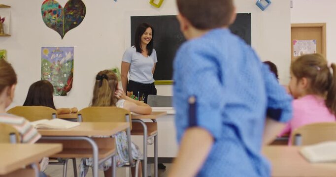 Attentive elementary school children learning in classroom as girl writes letters on blackboard with teacher s help, literacy lesson, primary education, modern school interior.