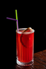 A tall glass of bright red fruit drink, garnished with a lime slice and fun straws