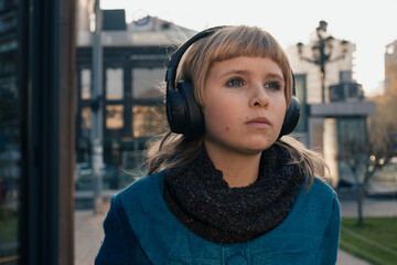 Teen girl listens to music on large wireless headphones outdoors
