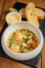 A bowl of flavorful shrimp soup adorned with herbs rests beside warm bread and butter