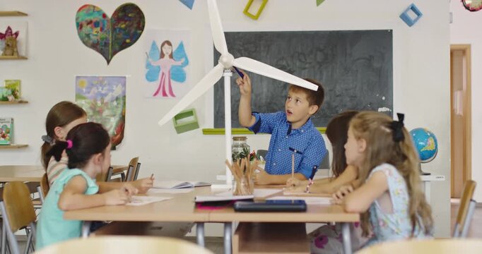 Curious schoolboy presenting wind turbine model to classmates in classroom, STEM lesson about renewable energy, science education and green technology for elementary children