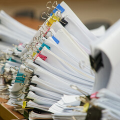 Huge stacks of sorted paper documents with colorful binder clips on a wooden office desk. Concept of bureaucracy and heavy administrative workload. Photo