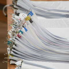 Huge stacks of sorted paper documents with colorful binder clips on a wooden office desk. Concept of bureaucracy and heavy administrative workload. Photo