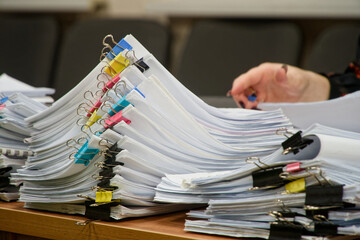 Huge stacks of sorted paper documents with colorful binder clips on a meeting table. Hand of a business woman working with an annual report or budget analysis. Photo