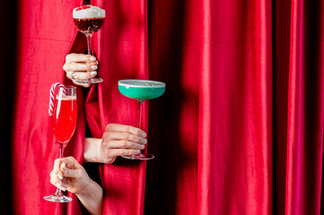 Three festive, colorful holiday cocktails, including one with a candy cane, are presented by hands...