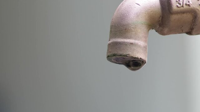 Water dripping from an old faucet, highlighting the preciousness of water and the importance of conservation. The faucet is a light color with signs of age and wear.