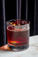 A vibrant cocktail on a marble table, glistening with ice and garnished with fruit