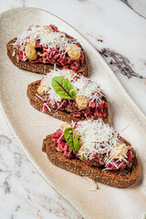 Savor the rich flavors of tartare on hearty brown bread, topped with fresh ingredients and cheese