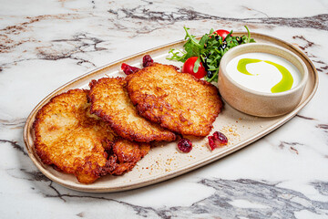 Delight in a plate of golden-brown potato pancakes accompanied by vibrant salad and a rich dip
