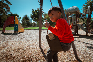 A child swings joyfully at a colorful playground under the bright sun