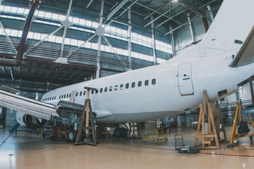 White passenger jetliner in the aviation hangar. Aircraft under maintenance. Checking mechanical systems for flight operations