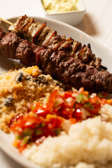 Macro close-up of mixed meat skewer with rice, farofa, and chopped peppers and onions.