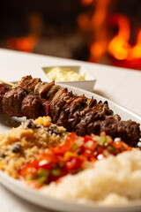Macro close-up of mixed meat skewer with rice, farofa, and chopped peppers and onions.