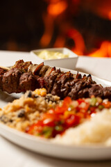 Macro close-up of mixed meat skewer with rice, farofa, and chopped peppers and onions.