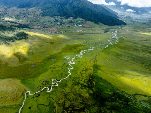 Aerial view of a serpentine river meanders through a vibrant green valley, contrasting with the dark shadows and distant mountains, Phobjikha Valley, Wangdue Phodrang, Bhutan. - Powered by Adobe