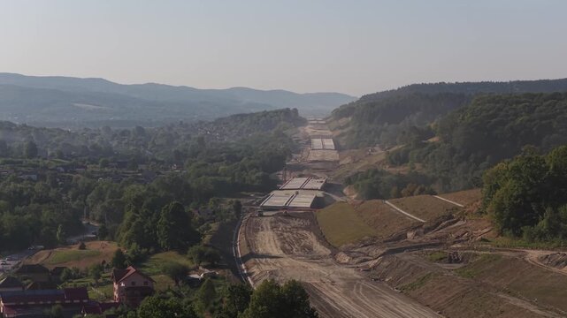 Highway construction in Romania 4k video. Aerial view of the A1 Motorway construction site near Curtea de Arges, showing an unfinished bridge over a valley and forested hills. Bucharest Sibiu road